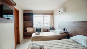 A hotel room with two beds, a desk, a TV, and a window with a city view. - Vallér Montanha Hotel (Lajeado)