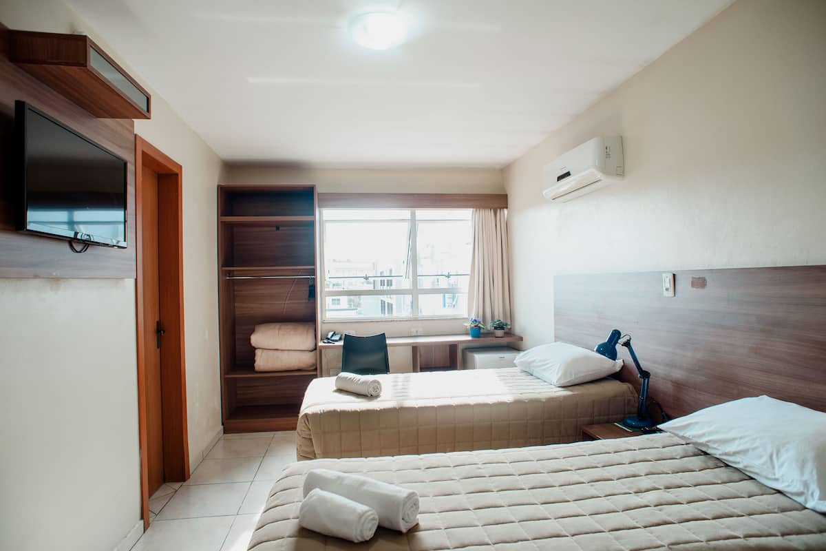 A hotel room with two beds, a desk, a TV, and a window with a city view.