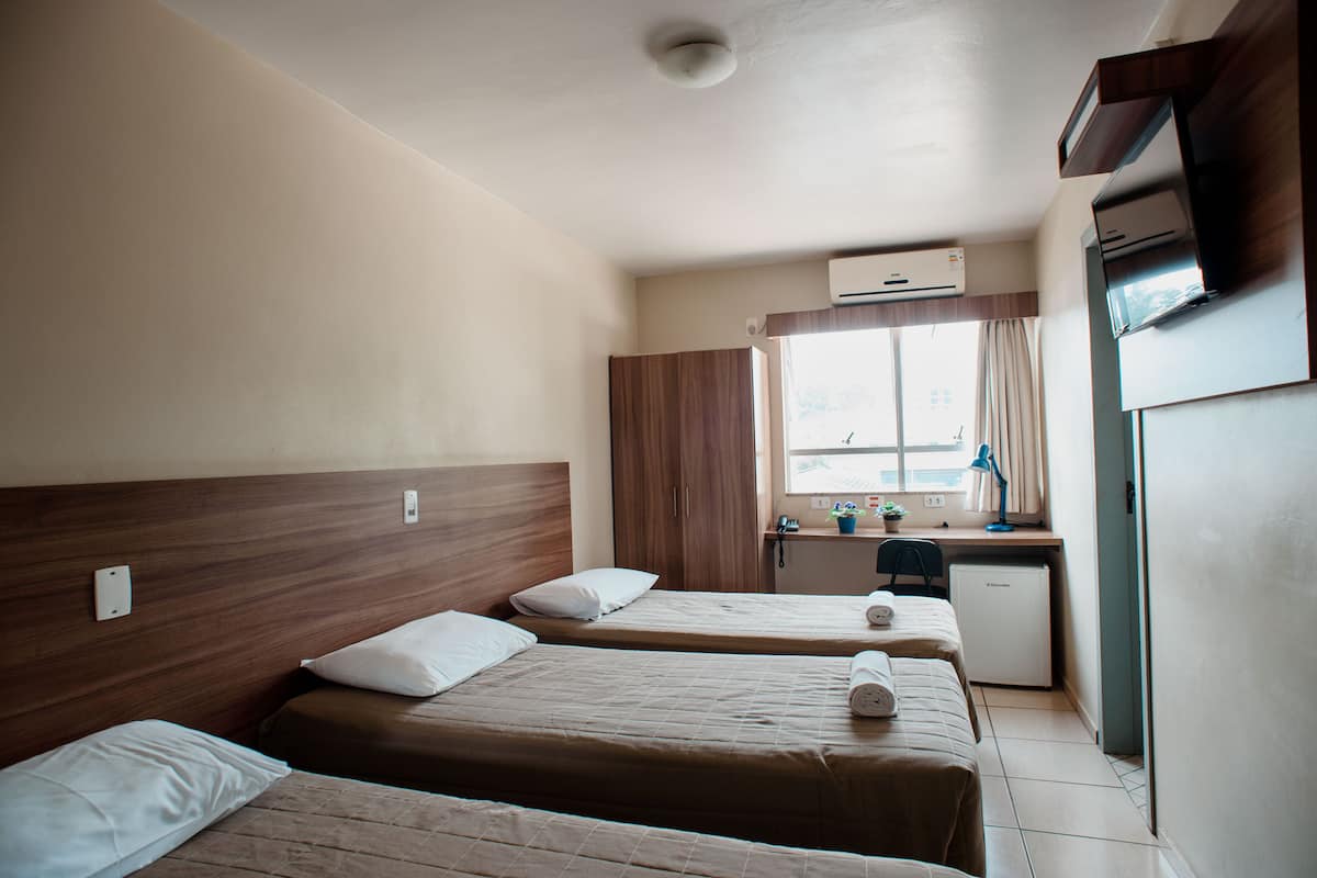 A hotel room with two beds, a small desk, a refrigerator, and a window with curtains.