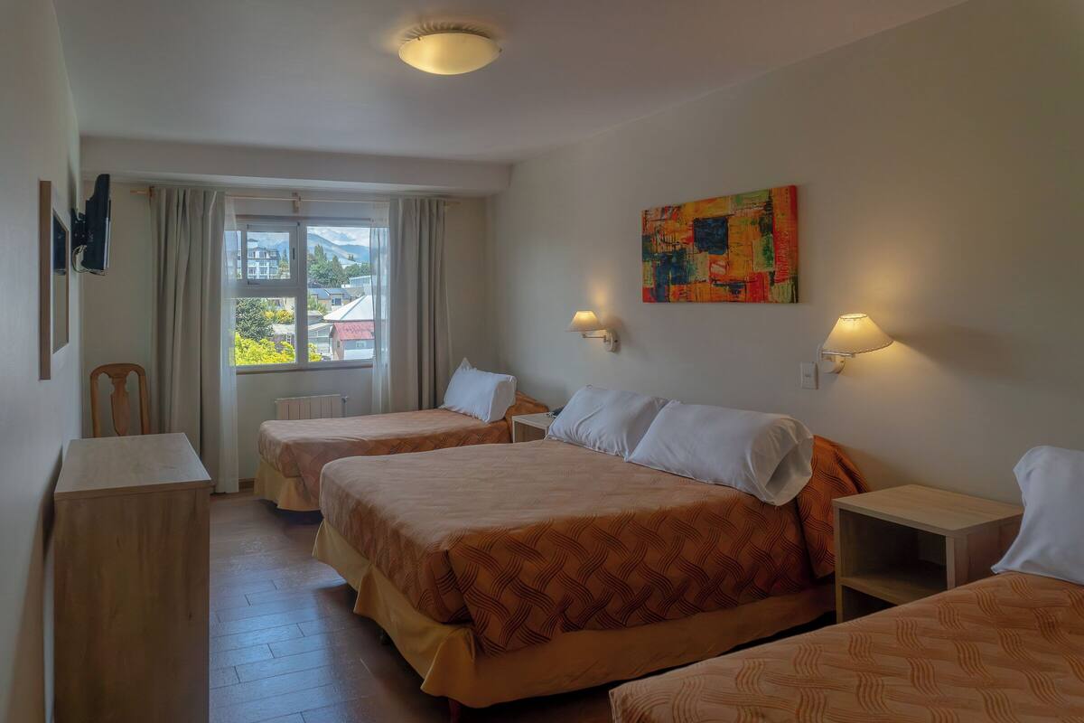 Ein Hotelzimmer mit zwei Betten, einem Holztisch, einem Fenster mit Vorhängen und einem Bild an der Wand.