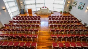 Ein großer Saal mit Reihen roter Stühle, die eine Bühne mit weißem Tischtuch zeigen.