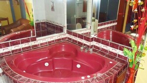 Un bagno con una vasca idromassaggio rossa, uno specchio grande e un vaso decorativo con piante.
