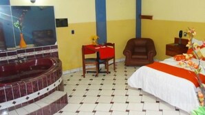 Camera d'albergo con un letto, una sedia, un tavolino, un divano rosso e bianco, una vasca da bagno e uno specchio.