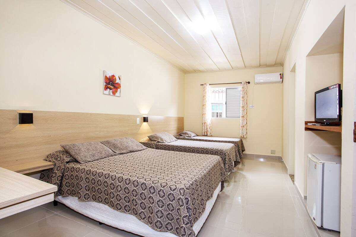 Habitación de hotel con dos camas, televisor, refrigerador pequeño y ventana con cortinas.