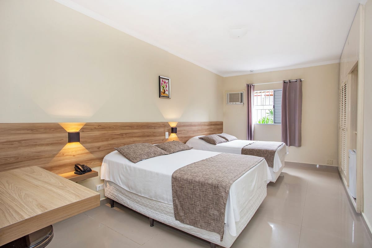 Habitación de hotel con dos camas, un escritorio de madera, una lámpara, un teléfono y una ventana con cortinas.