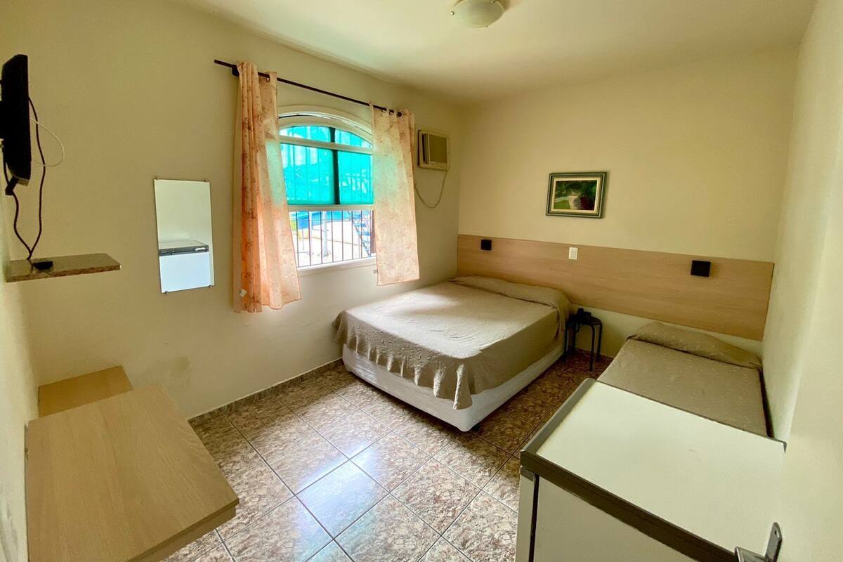 Una habitación pequeña y limpia con cama, escritorio, ventana con cortinas, televisor montado en la pared y luz en el techo.