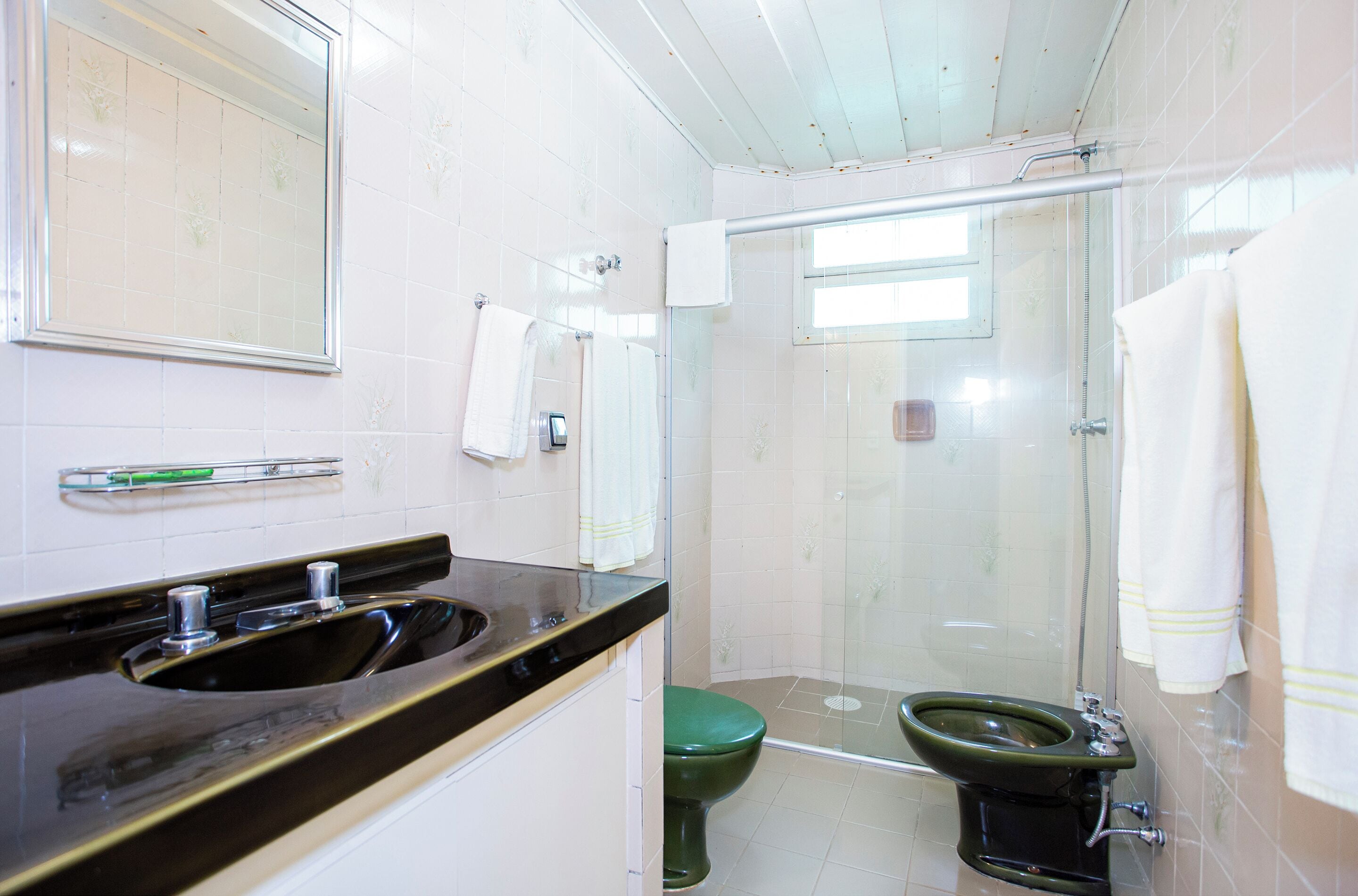 A bathroom with a black sink, a green toilet, and a glass-enclosed shower area.