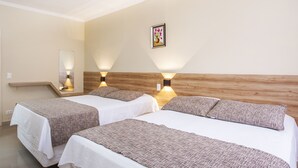 Quarto de hotel com duas camas, cabeceira de madeira, luminárias fixadas na parede e um quadro emoldurado.