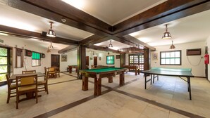 Um espaço amplo e interno com mesa de bilhar, diversos conjuntos de assentos e vigas de madeira no teto.