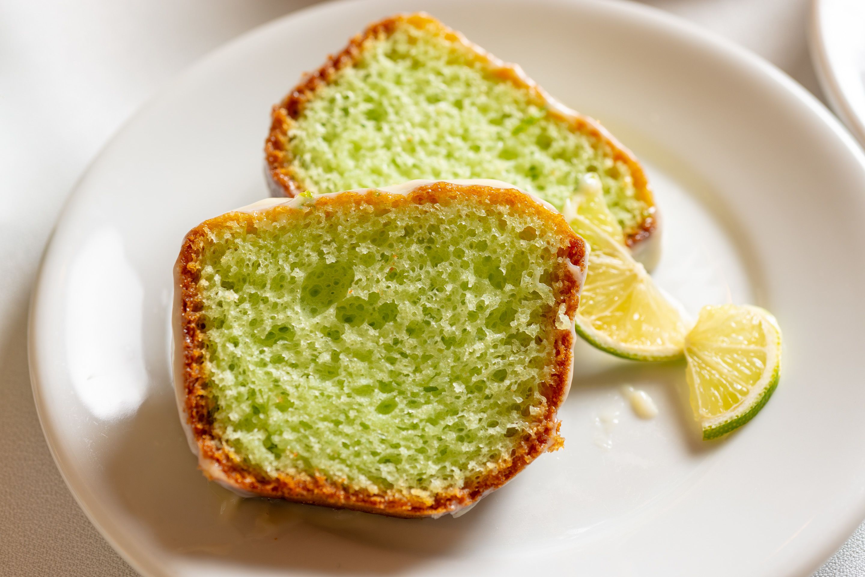 Dos porciones de pastel verde sobre un plato blanco, con un gajo de lima.