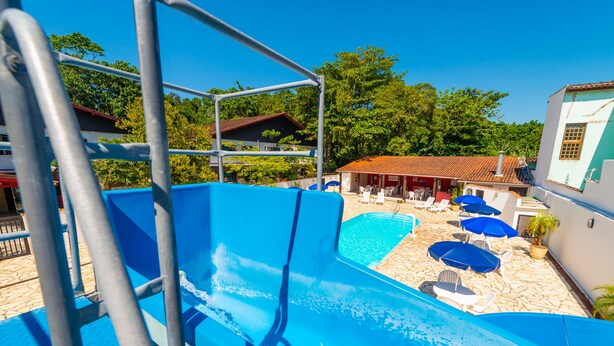 Piscina com um escorregador azul, rodeada por espreguiçadeiras e guarda-sóis.