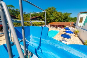 Una piscina con tobogán azul, rodeada de sillas de descanso y sombrillas.
