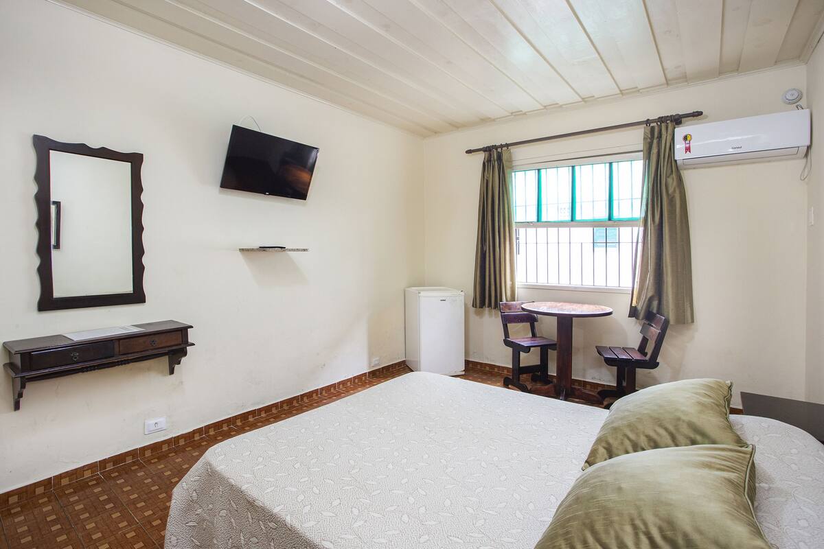 A room with a bed, a television, a small table, a chair, and a window with curtains.