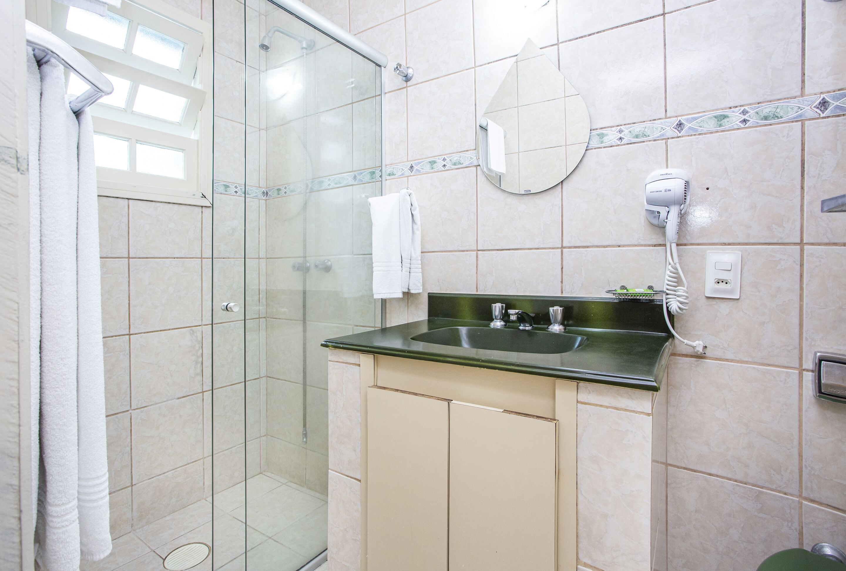 Un baño con cabina de ducha de vidrio, un lavabo con encimera verde y un secador de pelo en la pared.