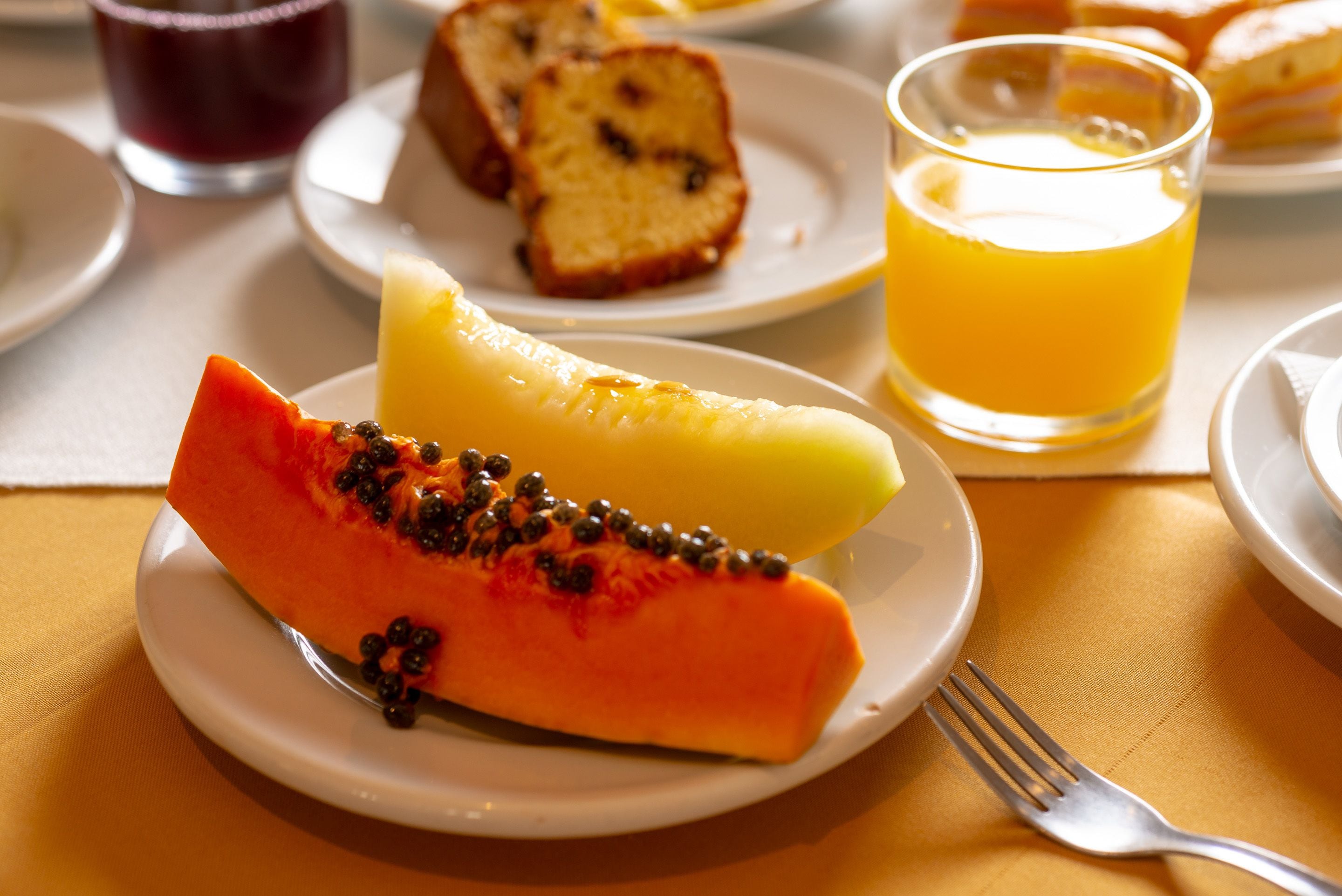Un plat amb una làmina de papaya i una banana, un got de suc d'aranja i una làmina de pa sobre una taula.