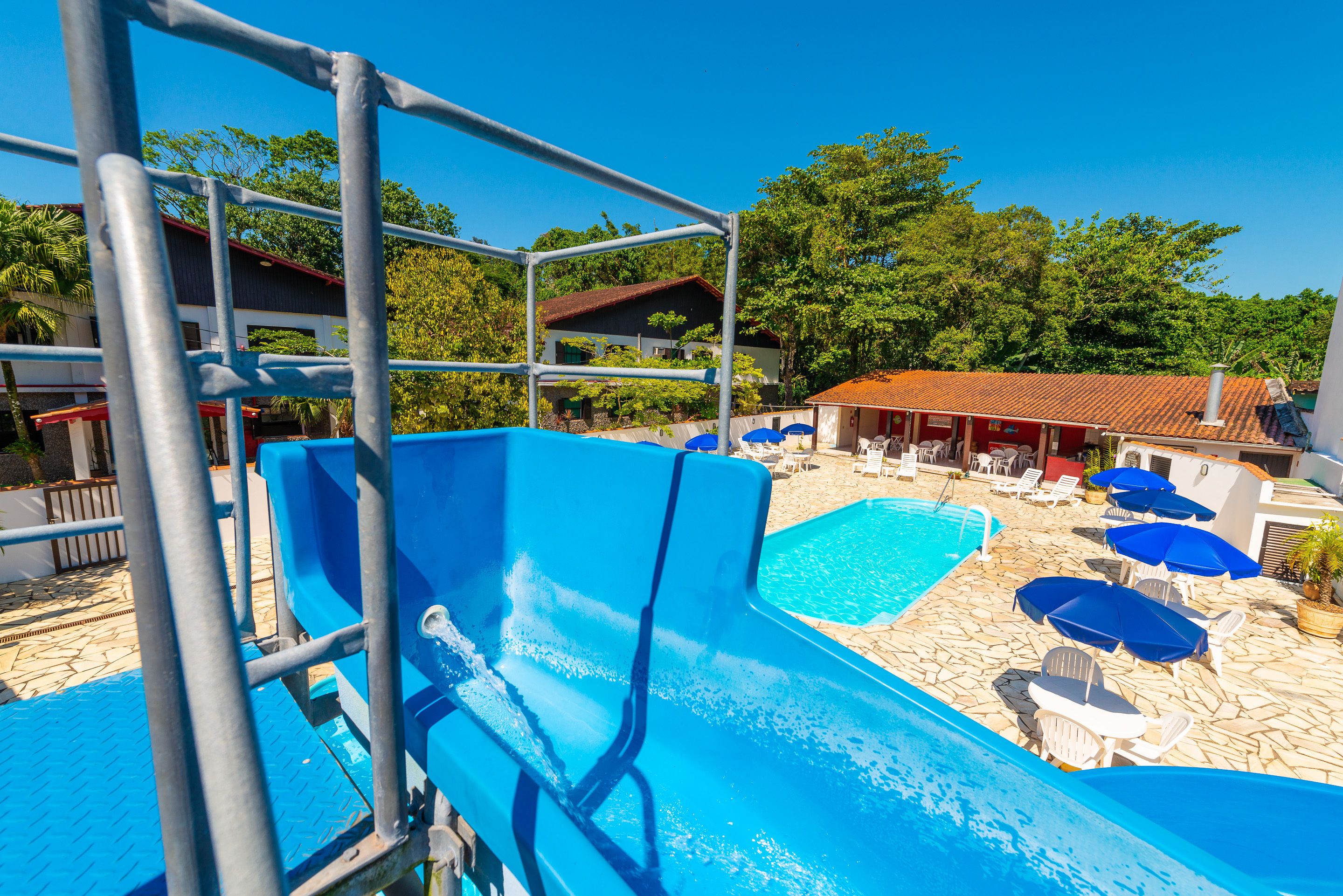 A pool area with a water slide, lounge chairs, and umbrellas.