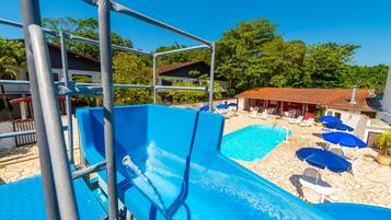 A pool area with a water slide, lounge chairs, and umbrellas.