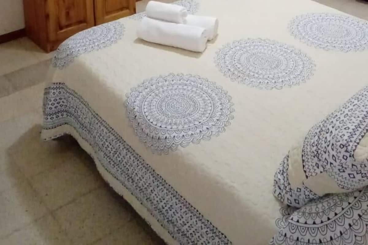 Une chambre à coucher avec un lit, un téléviseur posé sur un meuble en bois, un ventilateur de plafond et une porte avec des rideaux.
