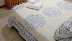 Un dormitorio con una cama, un televisor sobre un soporte de madera, un ventilador de techo y una puerta con cortinas.