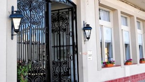Fachada de edificio con puertas de metal negras decoradas, una lámpara fijada a la pared y un cartel con el número de la dirección.