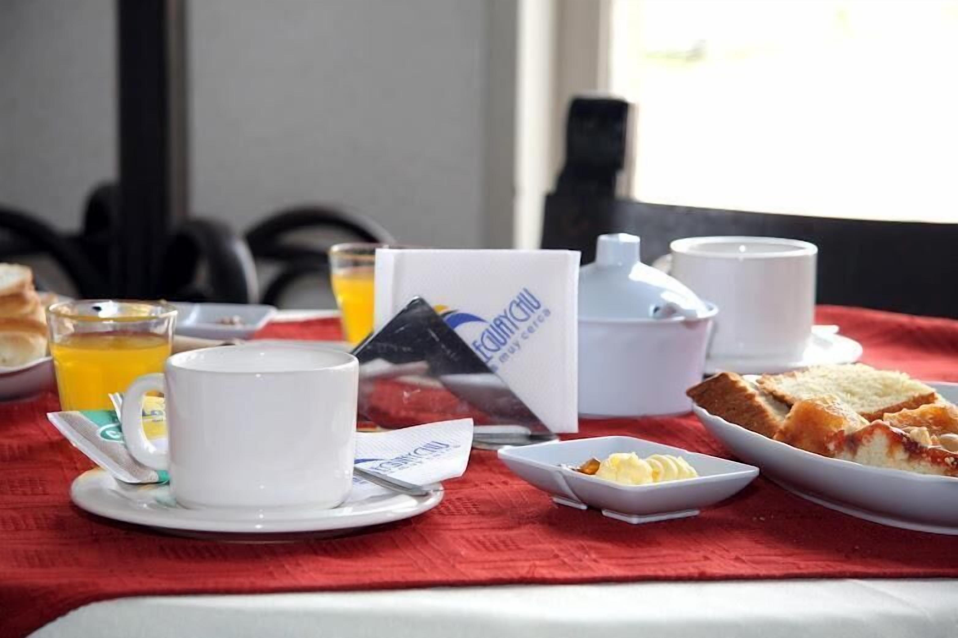 Une table dressée pour le petit-déjeuner avec une tasse, une théière, une tasse à thé, un verre de jus d’orange, un sachet de comprimés Equate et une assiette avec des toasts et du beurre.