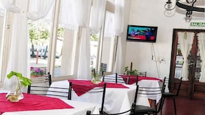 Un restaurante con mesas cubiertas con manteles blancos y posavasos rojos, un televisor montado en la pared y un letrero que dice "SALIDA" indicando la salida.