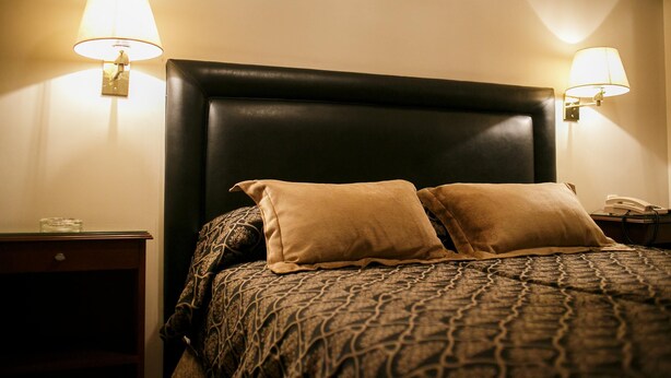 A neatly made bed with a patterned bedspread and two pillows, flanked by two bedside tables with lamps. - Hotel Presidente (San Miguel de Tucumán)