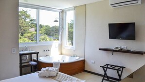 Un baño moderno con bañera, lavamanos e inodoro. Una ventana ofrece vistas a la vegetación exterior.