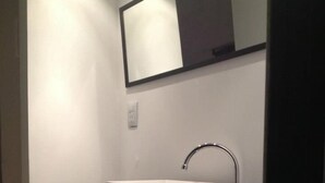 A bathroom with a white sink on a dark console table, a mirror above it, and a shelf below holding folded towels. - Alma Viva (Mar del Plata)