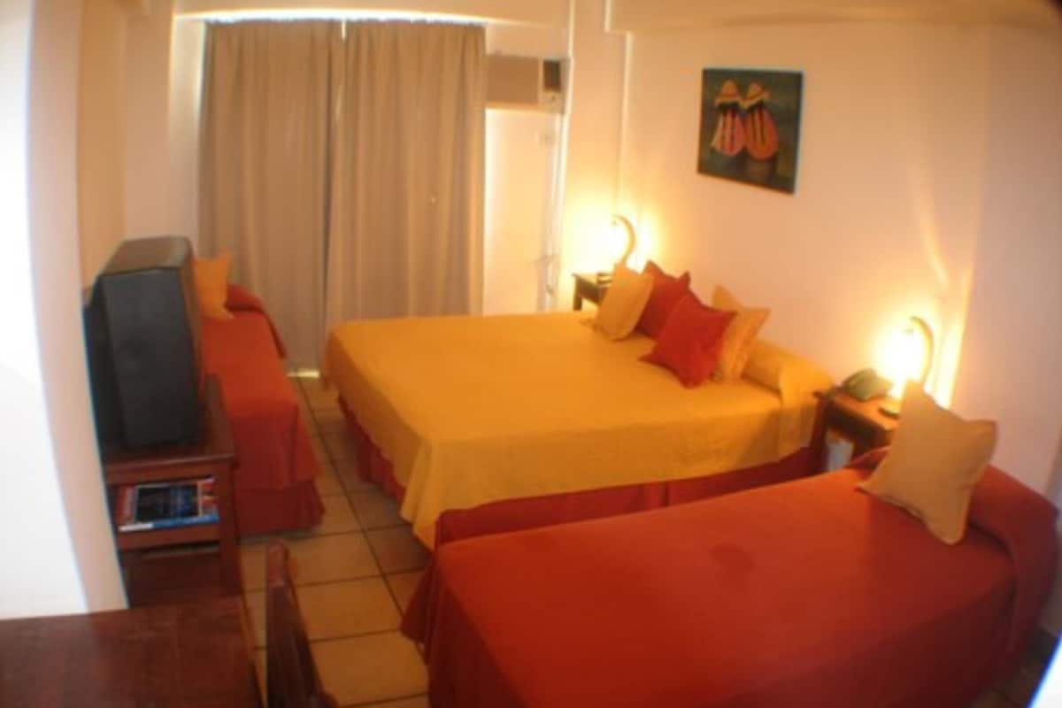A hotel room with a large bed, a smaller bed, a TV, and a desk with a lamp.