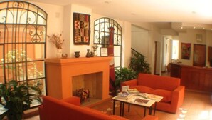 A living room with orange sofas, a fireplace, and a coffee table with magazines. - AltoParque Hotel (Salta)