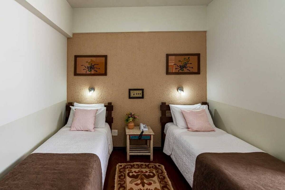 Habitació d'hotel amb dos llits individuals, una taula petita amb un telèfon i una catifa decorativa.