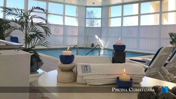 Un área de piscina interior con sillones de descanso, velas y vista a la piscina.