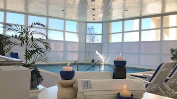 Un área de piscina interior con sillones de descanso, velas y vista a la piscina.
