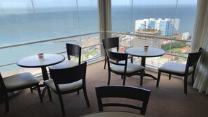 Un balcón con vistas al océano y a la ciudad, amueblado con mesas y sillas redondas.