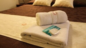 Een net opgemaakt bed met een gevouwen witte handdoek en een kleine fles lotion op een beige dekbed.