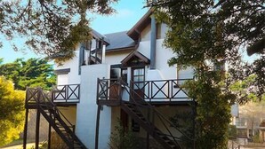 A modern two-story house with a balcony, a staircase, and a small garden area. - Cabañas Puerto Delfín (Mar de las Pampas)