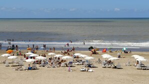 A beach with numerous white umbrellas and sun loungers, people swimming and walking along the shore. - Cabañas Puerto Delfín (Mar de las Pampas)