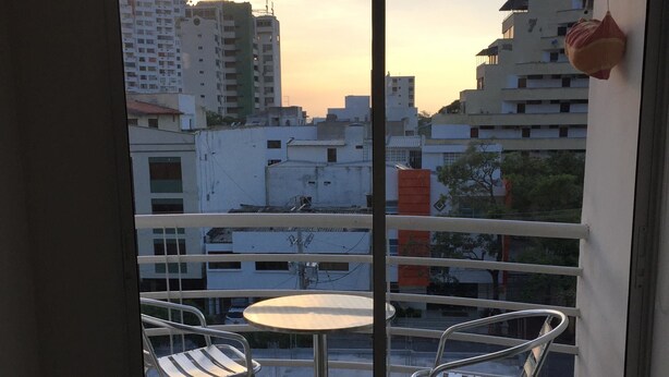 A balcony with a table and chairs, overlooking a cityscape with buildings and a sunset. - Edificio 7 Mares Apto 504 (Santa Marta)