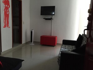 A living room with a flat-screen TV mounted on the wall, a red ottoman, and a patterned sofa. - Edificio 7 Mares Apto 504 (Santa Marta)