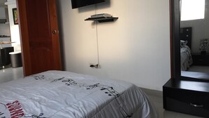 A bedroom with a bed, a TV mounted on the wall, a small shelf, and a door. - Edificio 7 Mares Apto 504 (Santa Marta)