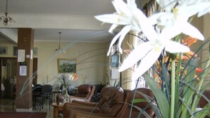A living room with leather sofas, a coffee table, and a vase with flowers. There is a dining area in the background with chairs and a table. - Hotel Sousas (Mar del Plata)