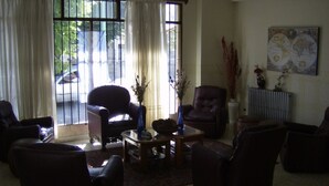A living room with two leather armchairs, a coffee table, and a radiator. There are curtains on the windows, and a painting on the wall. - Hotel Sousas (Mar del Plata)