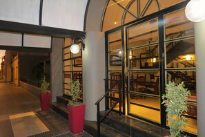 A hotel entrance with a glass door, a staircase, and potted plants.