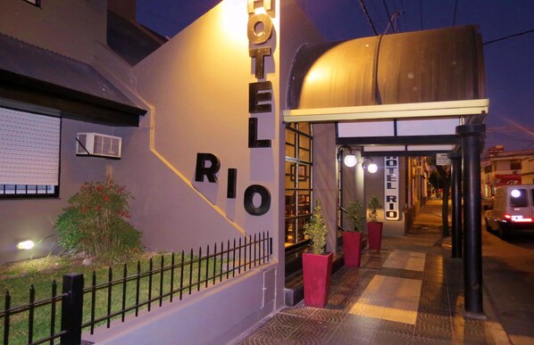 A hotel entrance with a sign reading "HOTEL RIO" and a covered walkway leading inside.