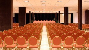 A conference room with rows of orange chairs, a stage with a black backdrop, and a podium. - Intersur Hotel 13 de Julio (Mar del Plata)