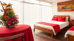 Camera d'albergo con due letti, una testiera in legno, un comodino, un tavolo con tovaglia rossa e un'interpretazione floreale.