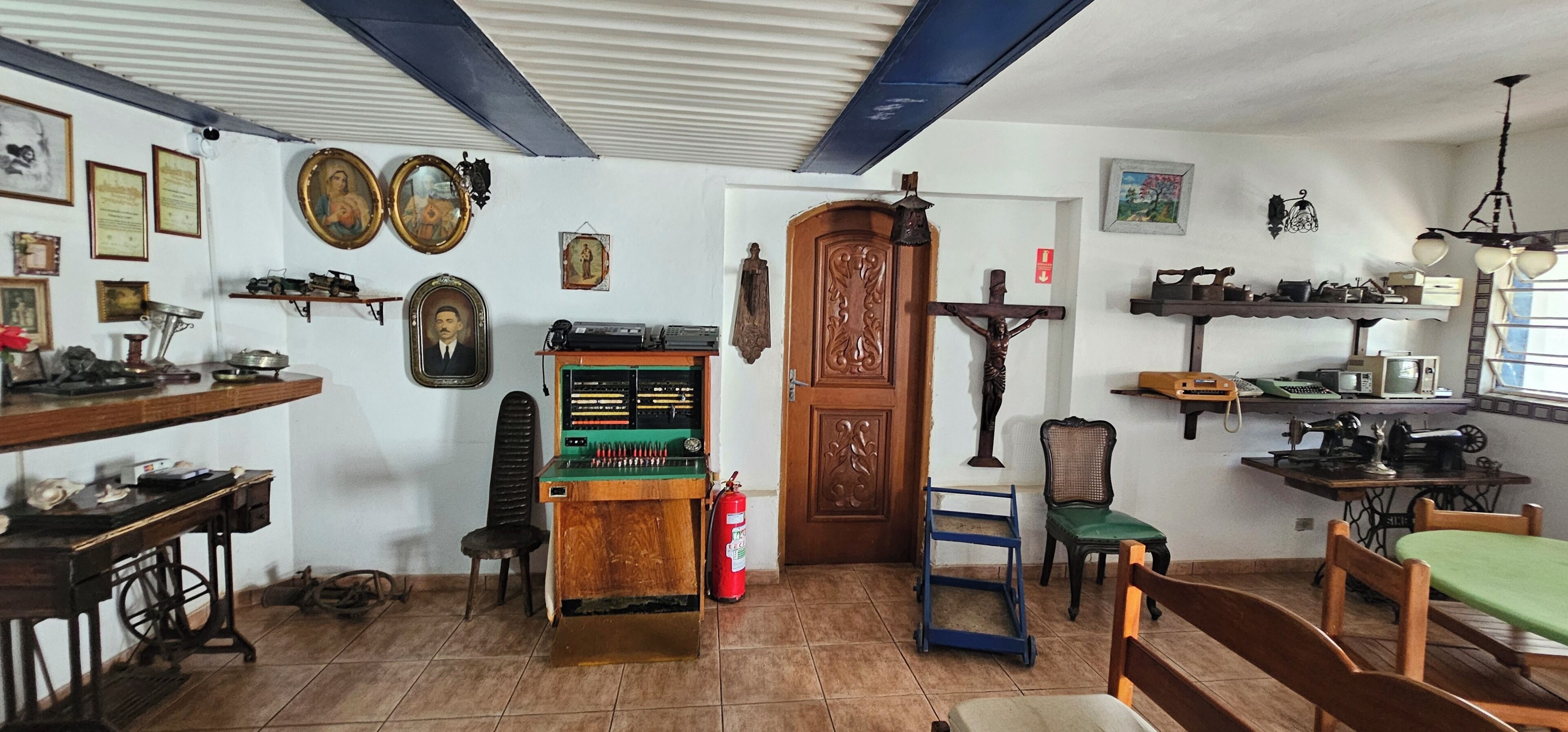 A room with a wooden door, a wooden chair, a small table, and a shelf with various items.