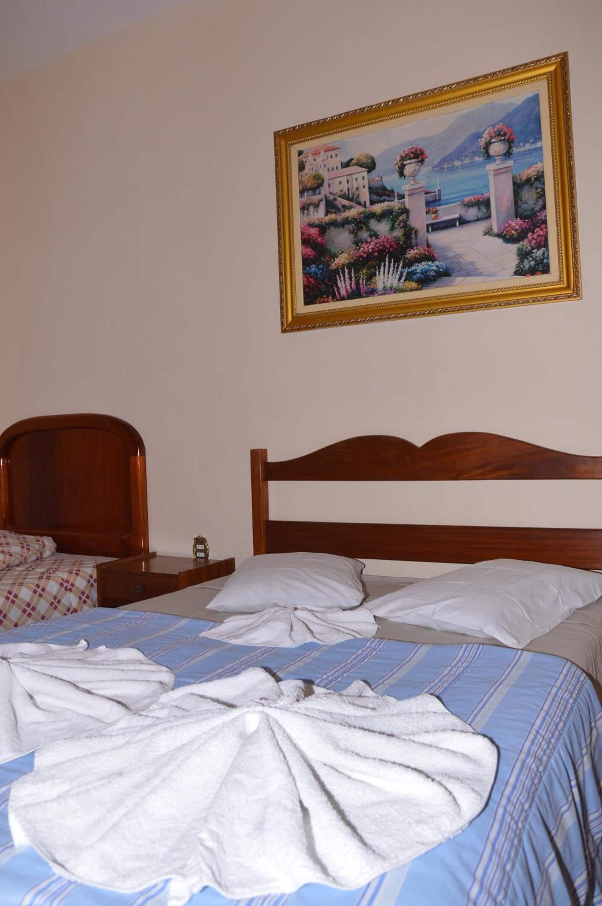 A hotel room with a wooden bed, a painting of a coastal scene, and a neatly made bed with towels.