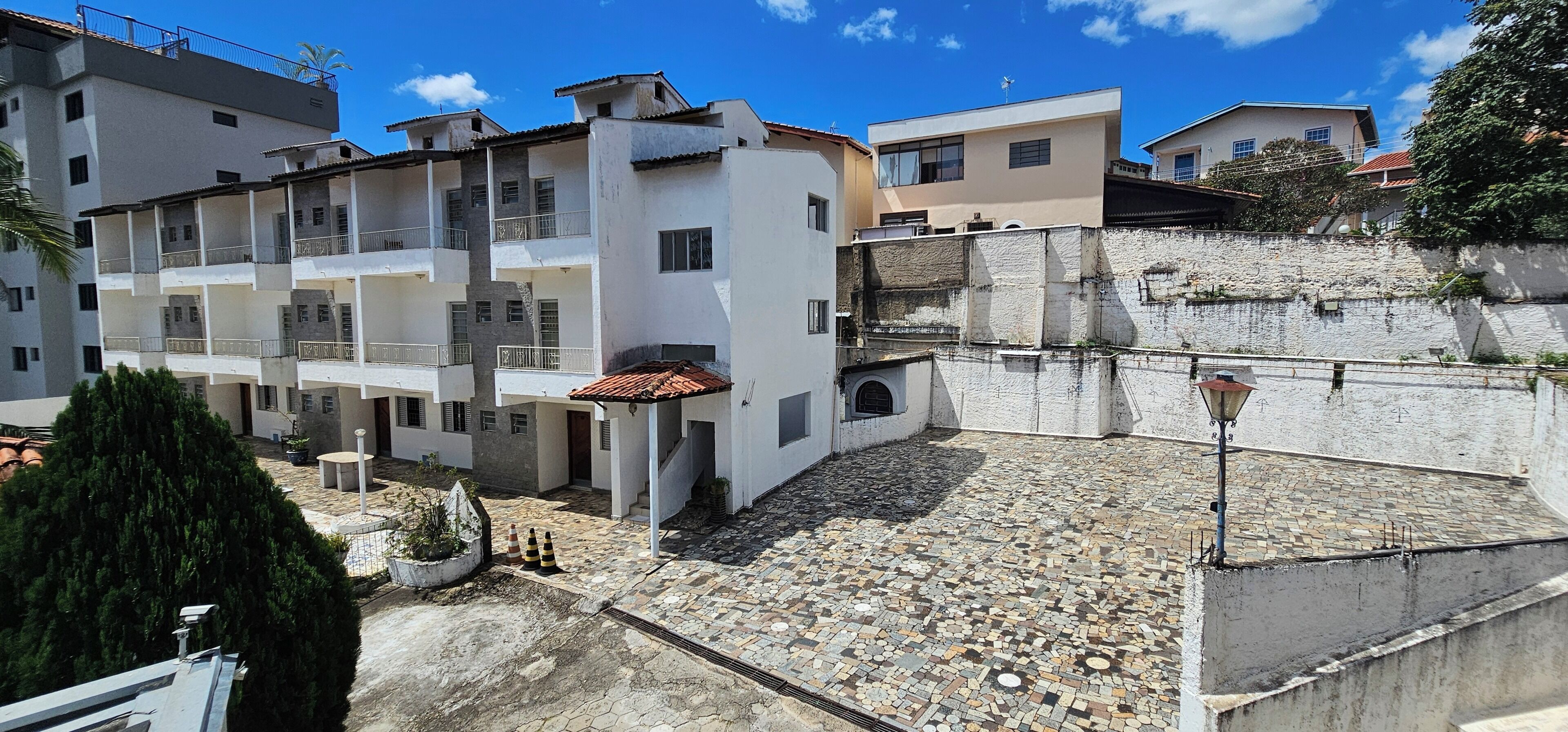 A multi-story residential building with balconies, a tiled courtyard, and a stone wall.